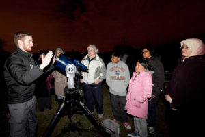 People standing with astronomer looking at telescope