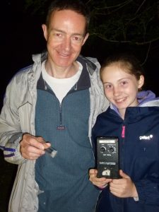 Two people holding a bat detector smiling at the camera